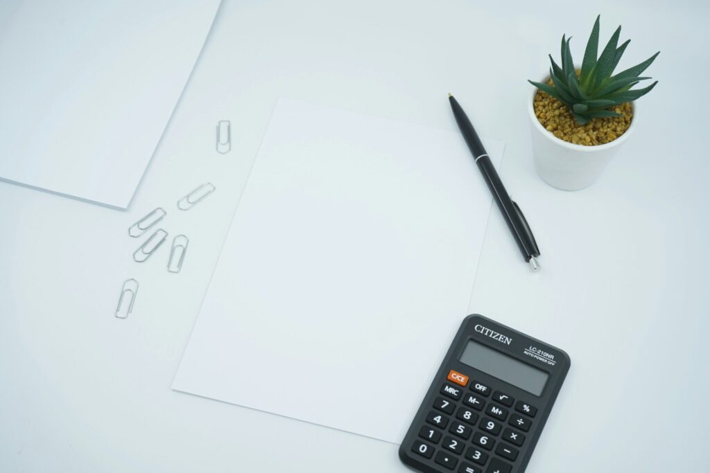 Blank paper, calculator, pen, and paper clip on white table